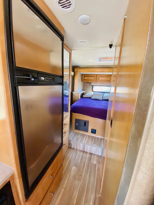 RV rental interior: stainless steel fridge, wood accents, and cozy bedroom with purple bedding.. Thor Motor Coach Other 2016