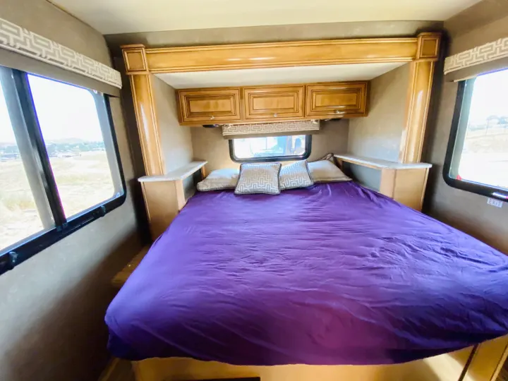 Spacious RV rental bedroom with a comfy purple bed, overhead cabinets, side shelves, and large windows.. Thor Motor Coach Other 2016
