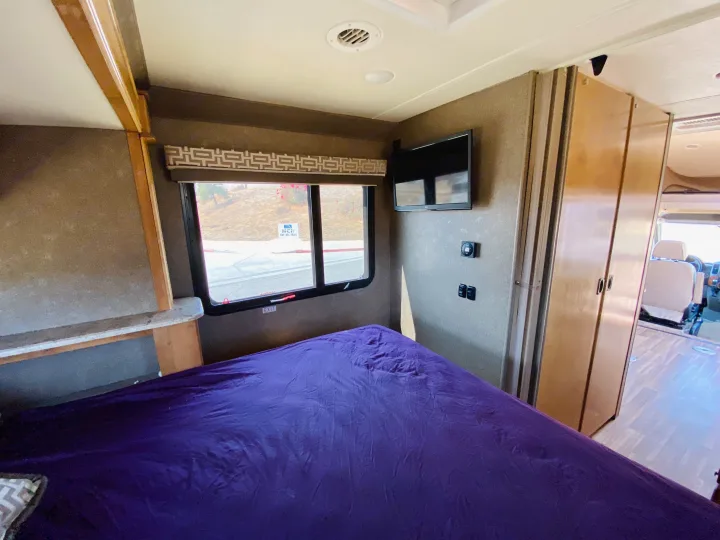 Experience comfort in this RV rental's bedroom, featuring a vibrant purple bed, TV, and scenic window view.. Thor Motor Coach Other 2016
