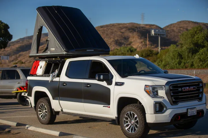 A white GMC Sierra AT4 pickup truck with a black hardshell rooftop tent, perfect for an adventurous RV rental.. Other Other 2021
