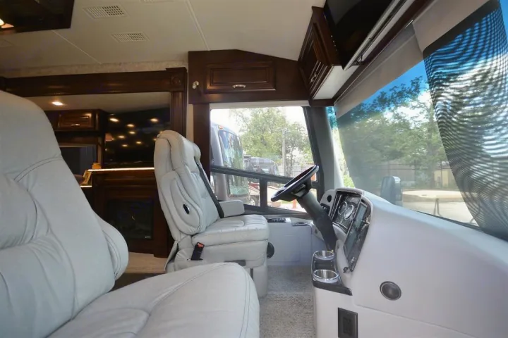 Spacious RV rental interior from the living area, showing light-colored captain's chairs, cockpit, and front window.. Entegra Coach Anthem 44B 2017