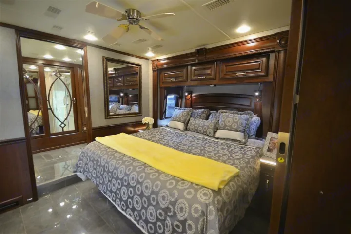 A luxurious RV bedroom with a large bed, dark wood furnishings, and overhead storage, ideal for your next RV rental trip.. Entegra Coach Anthem 44B 2017