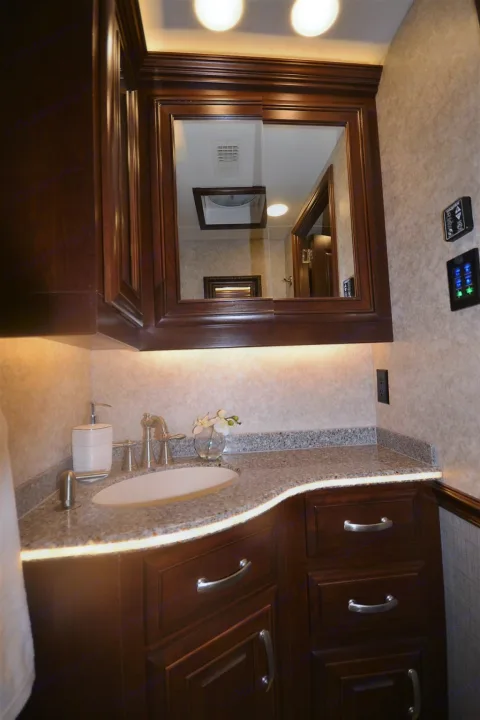 Luxurious RV rental bathroom vanity with dark wood, granite counter, modern sink, and elegant ambient lighting.. Entegra Coach Anthem 44B 2017