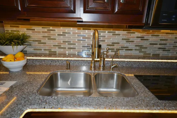 Well-equipped RV rental kitchen with a double sink, speckled counters, tiled backsplash, and under-cabinet lighting.. Entegra Coach Anthem 44B 2017