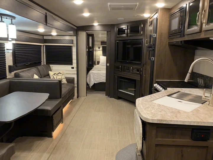 Bright rv rental interior featuring a modern kitchen, comfortable living area with a sofa, and a private bedroom.. Jayco White Hawk 2021