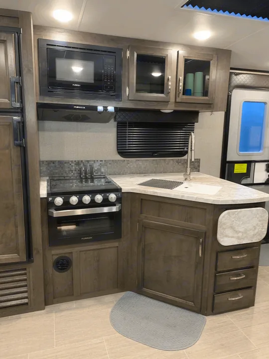 Modern RV rental kitchen with microwave, stove, sink, and wood cabinetry, ideal for your next adventure.. Jayco White Hawk 2021