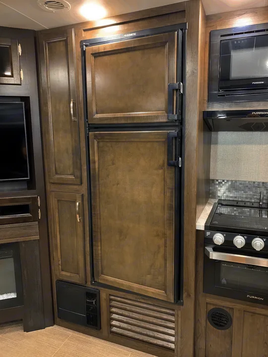 RV rental interior: wood-paneled Dometic refrigerator, Furrion microwave & stove in a functional kitchen space.. Jayco White Hawk 2021