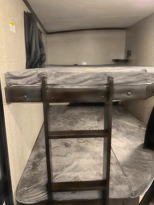 Inside an RV rental: close-up of dark bunk beds with grey blankets and a ladder for cozy travel accommodations.. Jayco White Hawk 2021