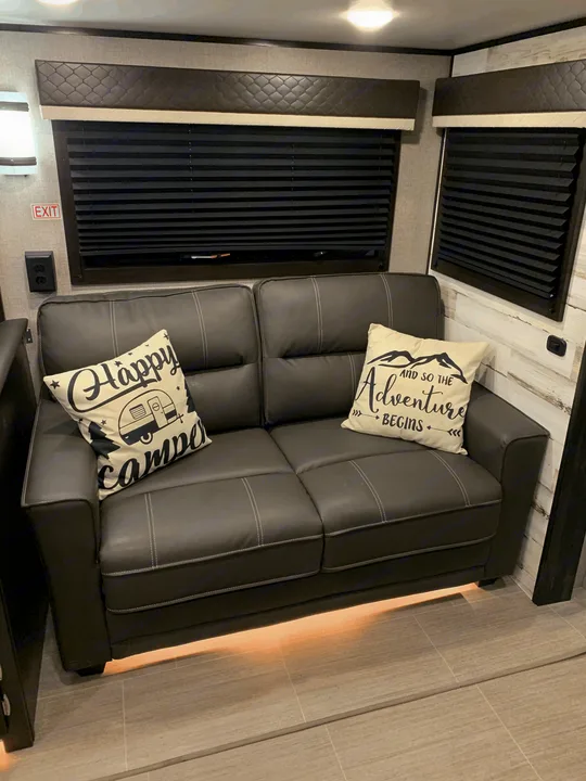 This inviting RV rental offers a comfortable dark sofa with accent pillows, modern window blinds, and subtle floor lighting.. Jayco White Hawk 2021