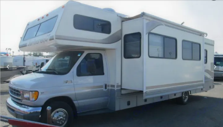 A white and silver Class C RV with its side slide-out extended, perfect for an rv rental experience.. Fleetwood Jamboree Sport 1999