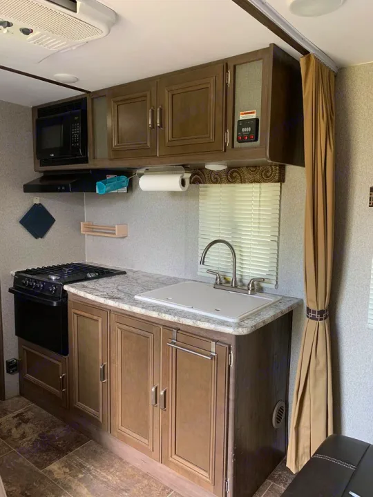 RV rental kitchen: A well-appointed space with a black stove, granite-look counter, sink, microwave, and wood cabinets.. Other Passport 2019