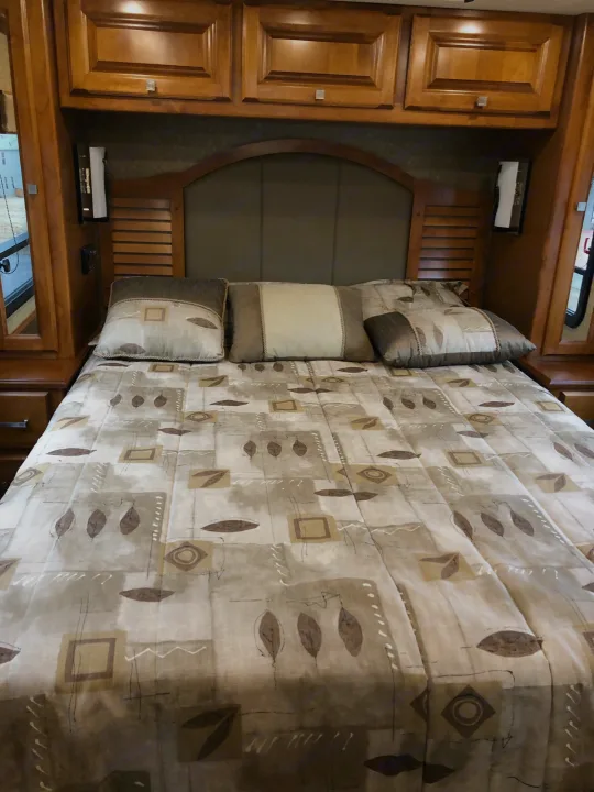 Cozy RV rental bedroom with a patterned comforter, decorative pillows, and ample wooden cabinetry.. Tiffin Motorhomes Allegro Breeze 32BR 2014
