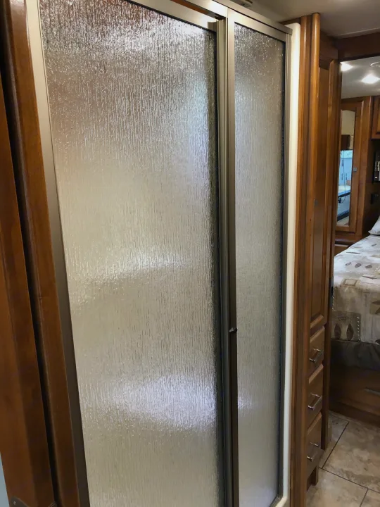 RV rental bathroom with textured glass shower door & wood cabinetry. Bedroom visible beyond.. Tiffin Motorhomes Allegro Breeze 32BR 2014