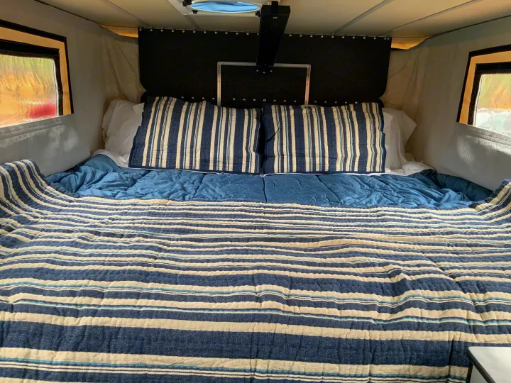 Step into comfort with this RV rental's cozy bedroom. Features blue & white striped bedding, pillows, & windows, perfect for travel.. Four Wheel Campers Other 2017