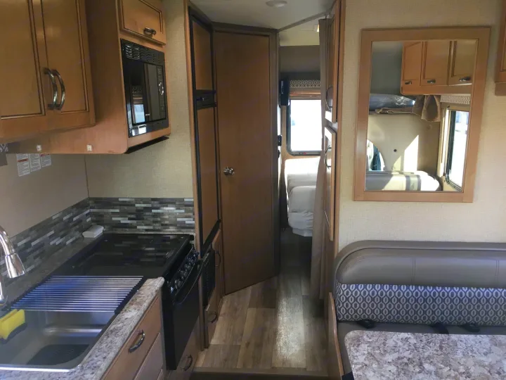 RV rental interior showing kitchen with stove/sink, dinette seating, and hallway leading to the bedroom area.. Thor Freedom Elite 2018