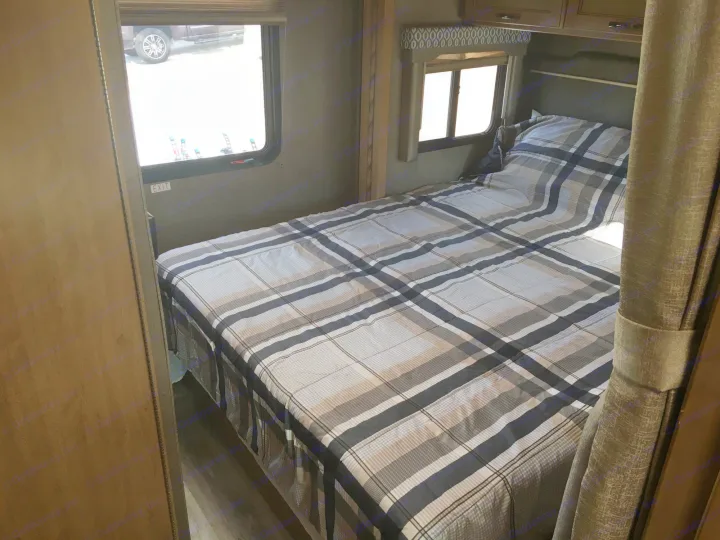 Interior of an RV rental: bedroom with a plaid bed, two windows, and an exit sign below one.. Thor Freedom Elite 2018