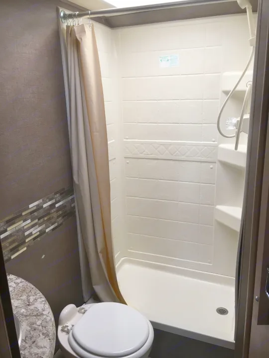 RV rental bathroom: A compact space with a bright, white shower, beige curtain, and toilet. Perfect for on-the-go living.. Thor Freedom Elite 2018