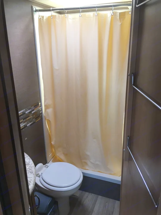 Inside an RV rental: a compact bathroom featuring a toilet, a light-colored shower curtain, and a towel bar.. Thor Freedom Elite 2018