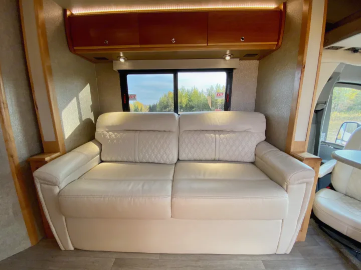 RV rental interior: A light-colored sofa with diamond stitching, overhead cabinets, and a window looking out at trees.. Wayfarer Wayfarer Motorhome 2017