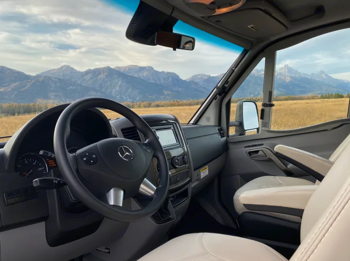 Interior of an RV rental: a Mercedes-Benz dashboard, steering wheel, and a scenic mountain view outside. Ready for adventure.. Wayfarer Wayfarer Motorhome 2017