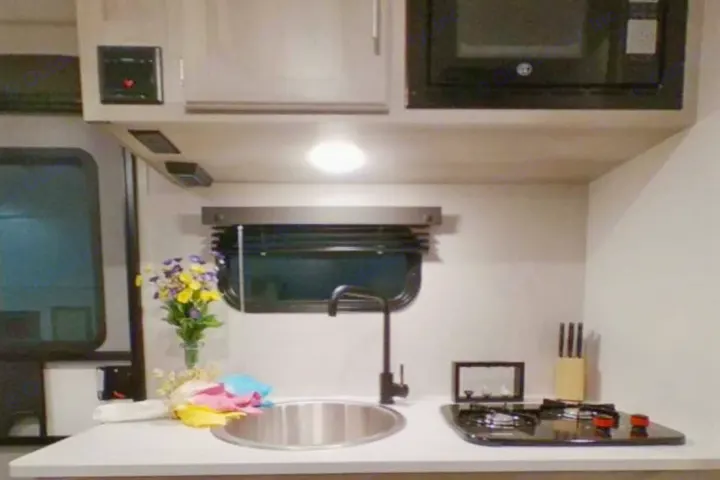 Compact RV rental kitchen features a sink, faucet, two-burner stove, microwave, and cabinets for your travels.. K-Z Manufacturing Escape 191bhk 2021