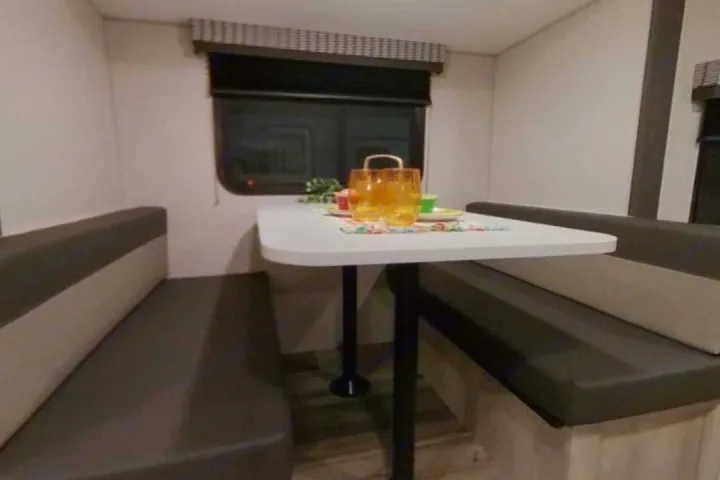 RV rental dinette: a cozy booth with table, set with glasses & placemat, beside a window. Perfect for meals.. K-Z Manufacturing Escape 191bhk 2021