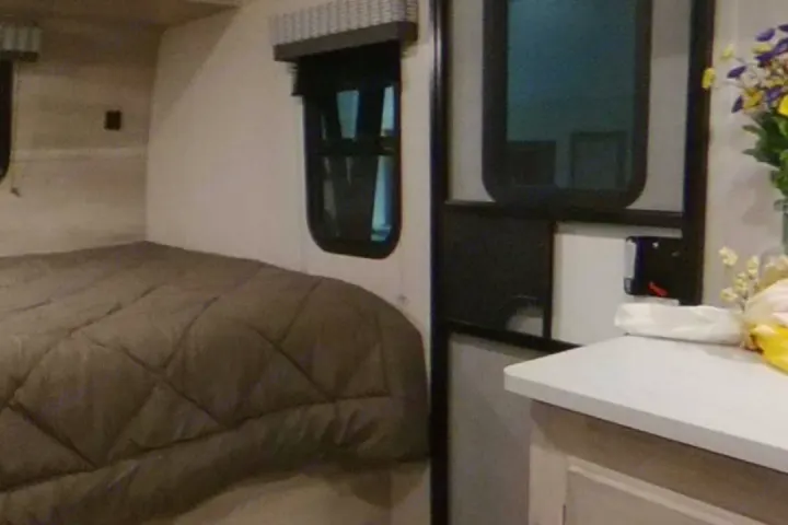 RV rental interior showing a cozy quilted bed, window with blind, and compact counter. Perfect for travel comfort.. K-Z Manufacturing Escape 2021