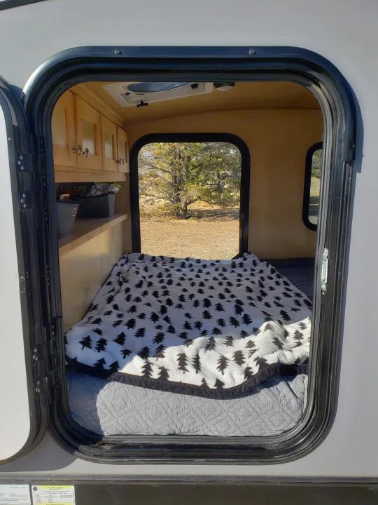 Cozy rv rental interior: A compact camper with a bed, tree-patterned blanket, cabinets, and a window view of nature.. Escapade Ridge 2018
