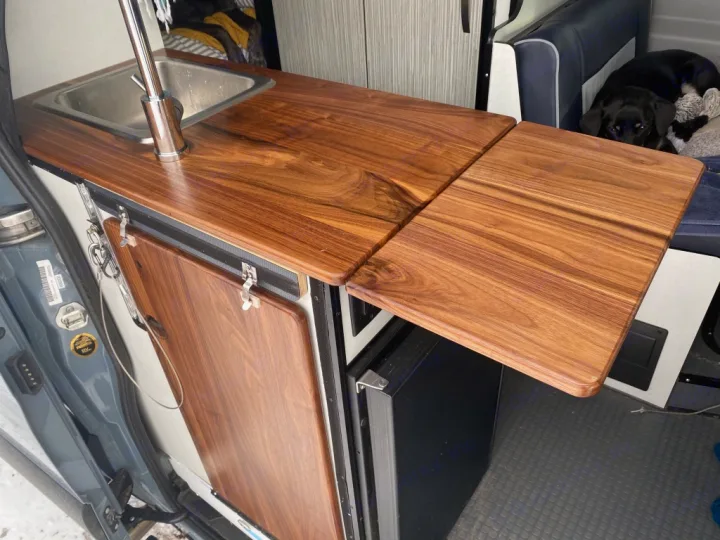 Efficient RV rental camper van kitchen: wood counter, sink, and extendable workspace. A cozy spot for canine friends.. Winnebago Revel 2021