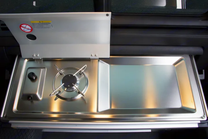 Sleek stainless steel kitchen in an RV rental, featuring a single gas burner, sink, and safety cover for camping adventures.. Volkswagen Transporter California Beach 2019