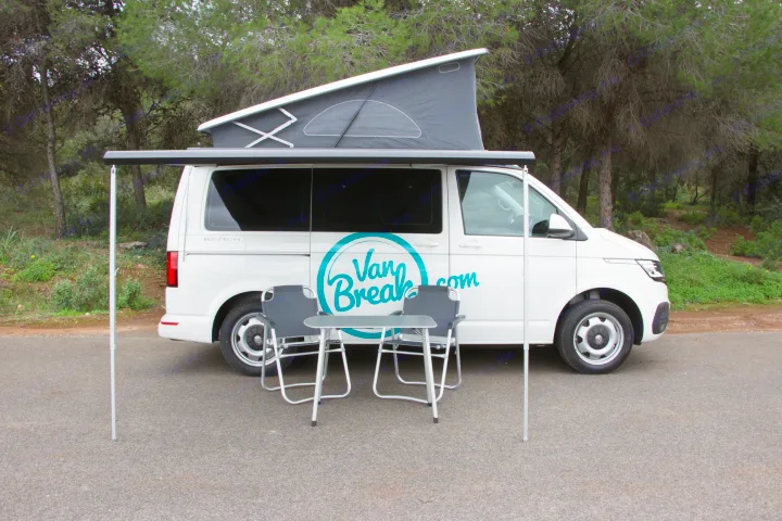 White camper van (VW-style) for RV rental, with pop-top roof, extended awning, and outdoor table/chairs setup.. Volkswagen Transporter California Beach 2019