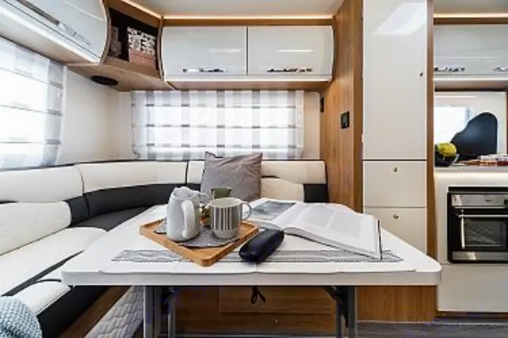 This modern RV rental features a bright camper interior with a comfortable U-shaped dining area, a table, and a functional kitchen.. Ford Rollerteam 747 2026