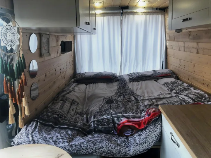 Stylish RV rental featuring a Parisian-themed bed, wood-paneled walls, and built-in storage for comfy travels.. Ford Transit 2015