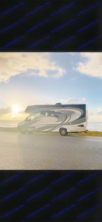 An RV rental motorhome with a sleek design is parked on a road next to the ocean at sunset, ideal for a scenic road trip.. Coachmen Prism 2019