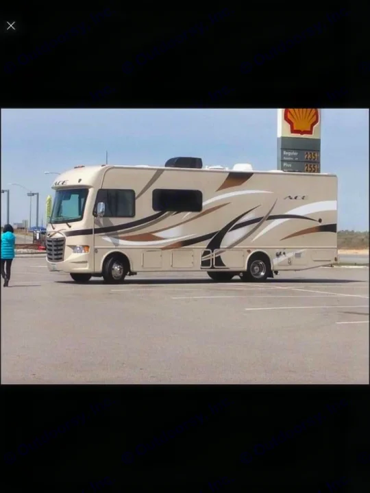 Spacious RV rental, light tan with brown swirls, parked at a Shell gas station under clear skies.. Thor Motor Coach A.C.E 2015