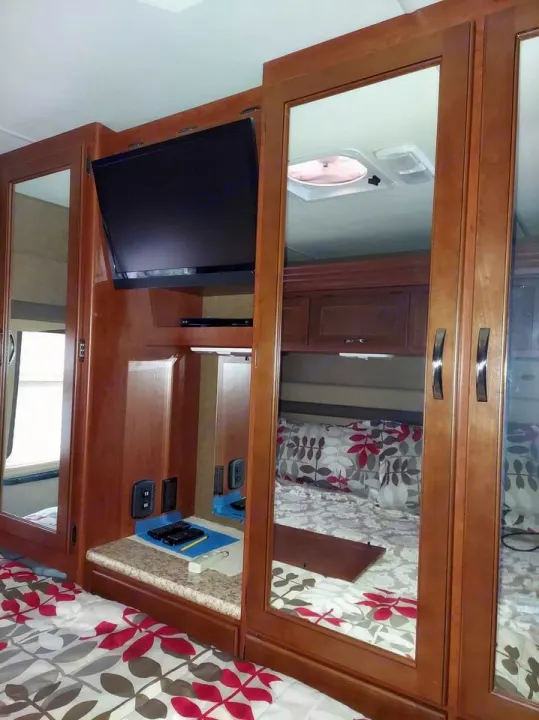 This RV rental bedroom features a TV, ample mirrored storage, and a comfy bed with floral sheets for your travels.. Thor Motor Coach A.C.E 2015