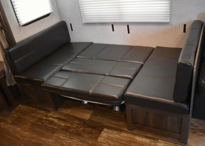 RV rental dinette converts to a bed, showing dark leather cushions and wood-look flooring for versatile use.. Starcraft Autumn Ridge 2020
