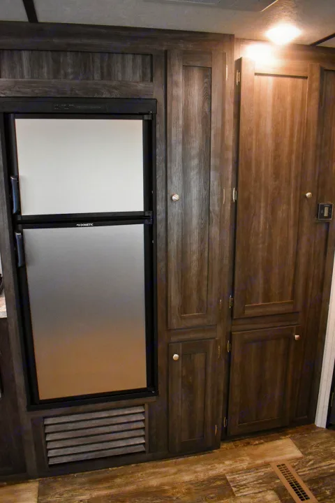 RV rental interior with a Dometic two-door refrigerator and built-in dark wood-grain storage cabinets, providing essential space.. Starcraft Autumn Ridge 2020