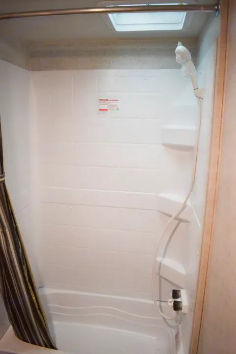 Clean RV rental shower features white walls, tub, curtain, and a wrapped handheld shower head, perfect for travel.. Starcraft Autumn Ridge 2020