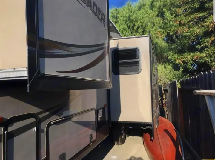 Side of an RV rental travel trailer (Crusader) with slide-outs extended, parked by a fence and red canoe.. Forest River Crusader 2015
