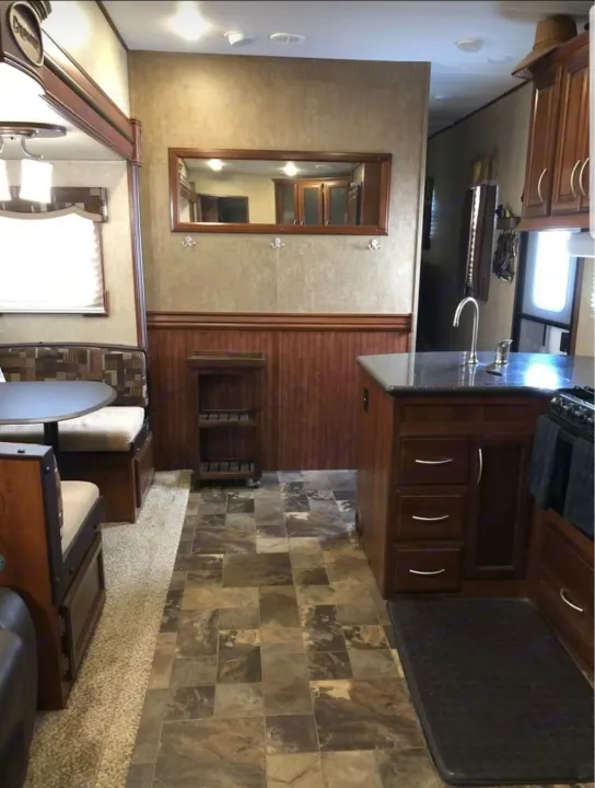 RV rental interior: cozy dining booth, full kitchen with sink & cabinets, wood paneling, and tiled floors.. Forest River Crusader 2015