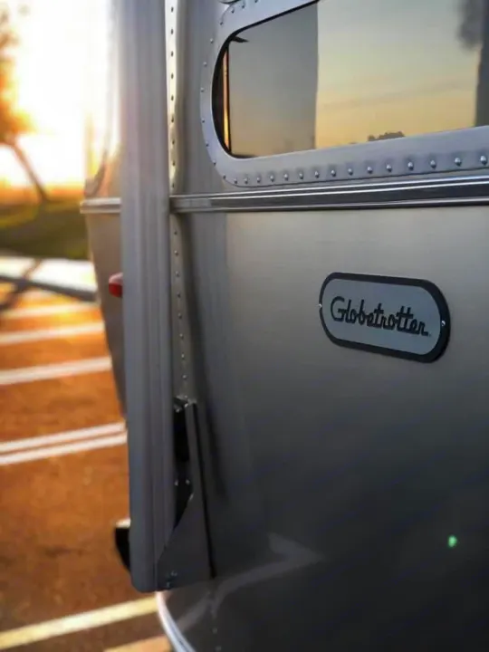 Close-up of a shiny Airstream Globetrotter RV rental, showcasing its iconic riveted aluminum body and distinctive oval window.. Airstream Globetrotter 2020