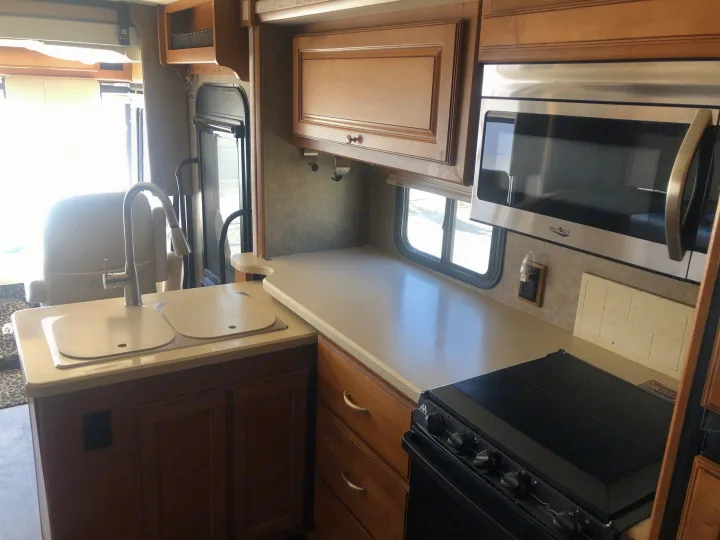 Bright RV rental kitchen with light countertops, dual sink, stainless microwave, black stove, and wood cabinets.. Itasca Sunstar 2015