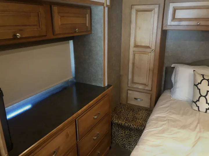 RV rental bedroom with wooden cabinets, a desk with blue under-lighting, a bed, and leopard print storage ottoman.. Itasca Sunstar 2015