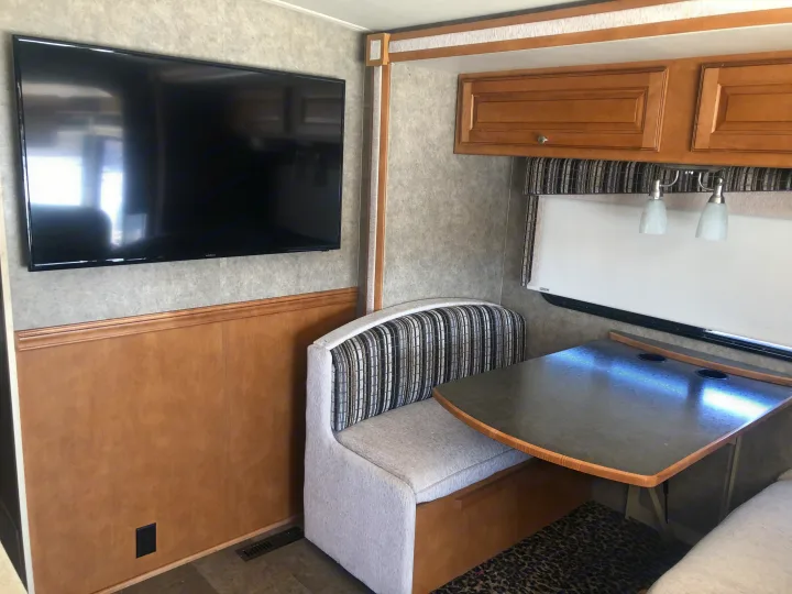 Cozy RV rental dinette area with striped bench seating, a mounted TV, and wood cabinets.. Itasca Sunstar 2015