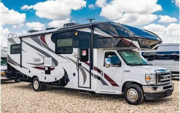 White and black Class C RV rental with bold graphics, parked on a gravel lot under a blue sky. Perfect for travel adventures.. Entegra Coach Esteem 2021