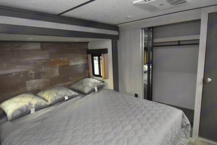 RV rental bedroom interior: light grey bed with patterned pillows, wood-look headboard, and sliding closet.. Other Montana High Country 2021