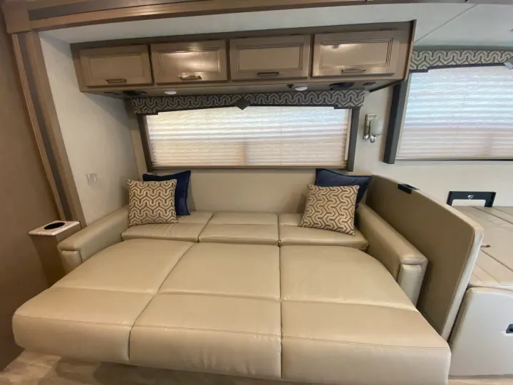 This RV rental features a cozy, light-colored sofa that converts into a bed, offering comfort with overhead storage and window blinds.. Thor Motor Coach Hurricane 2021