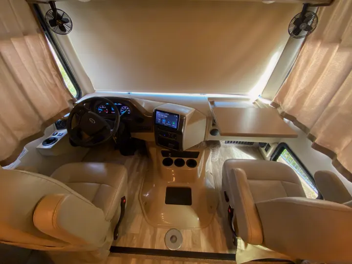Spacious RV rental cockpit: driver/passenger seats, dashboard with infotainment screen, and pull-out table. Ideal for an RV trip.. Thor Motor Coach Hurricane 2021