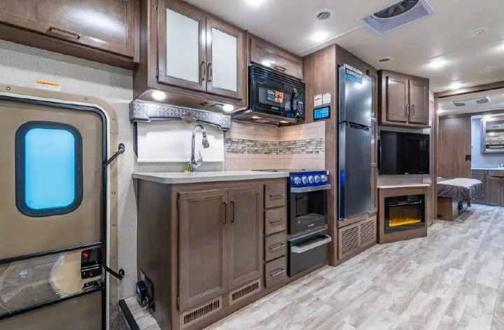 Well-equipped rv rental kitchen & living space. Features a microwave, oven, sink, fridge, TV, & electric fireplace.. Thor Motor Coach Hurricane 2021